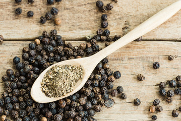 grounded black pepper in wooden spoon on black pepper and wood texture background, close up