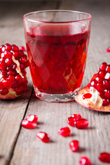 Broken red ripe juicy pomegranates and glass of fresh juice on rustic wooden unpainted table