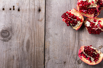Broken red ripe juicy pomegranates on rustic wooden unpainted table