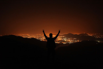 Young man on top of the hill observing the night city view.