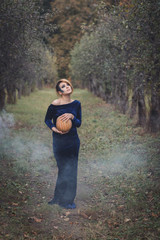Young woman in a dress in the autumn garden. She is holding a pumpkin