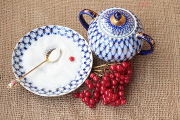 Bunch of red viburnum. Saucer with sugar and sugar bowl on sacki