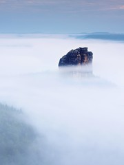 Sharp sandstone rock empire sticking out from heavy fog. Deep misty valley