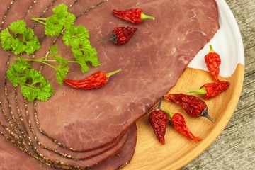 Cold roast beef on a wooden table. Delicacy of beef. Preparing cold refreshments. Traditional meal. Beef roast beef with green pepper and chili peppers.
