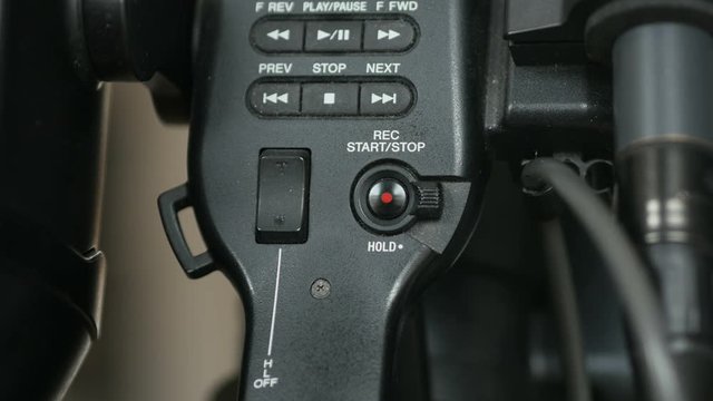 Pressing the top handle record button on an ENG video camera.