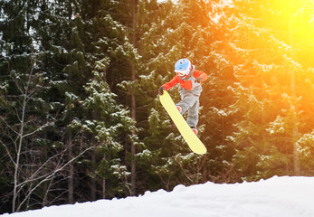 Boy jumping and keeps one hand on the snowboard in the mountains with snow-covered firs in...