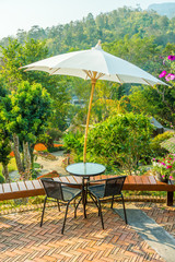 Modern round table and wicker chairs with sun shade umbrella. They are on a terrace or patio.
