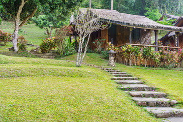 Retro Thai home and concrete walkway in a yard. The house is on a foothills.