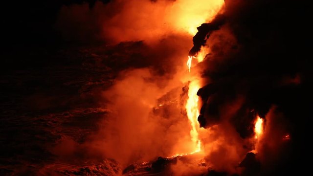 Lava reaches ocean from lava stream on Big Island Hawaii. Lava running into pacific ocean and red hot glowing lava rocks flowing out with waves. Dramatic amazing nature landscape. Volcanic eruption.