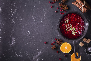 Fresh homemade cranberry sauce in a pan on dark wooden background with scattering of ripe berries.