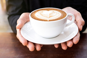 Morning coffee, hands holding cup of hot coffee latte with heart
