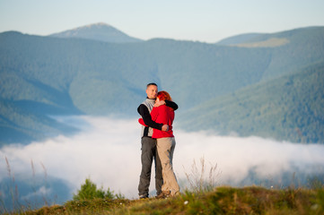 Fototapeta na wymiar Happy couple embracing against beautiful mountain landscape with morning haze over the mountains and forests