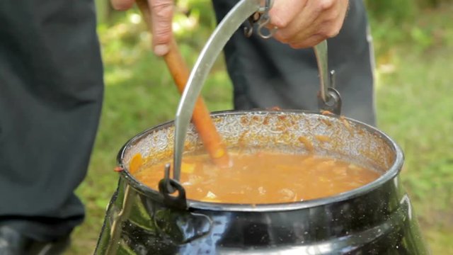close-up of a boiling goulash soup in a vintage kettle hanging over a campfire