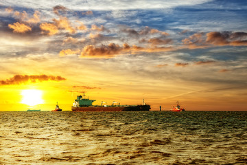 Fototapeta na wymiar Tanker ship with escorting tugs on sea at sunrise.