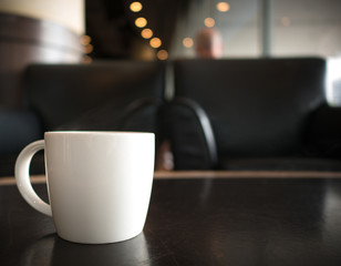 white cup of hot americano on dark brown table, empty sofa and light bokeh on background, 