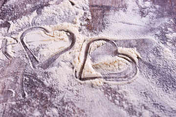 Heart from a cookie cutter in flour on wooden table