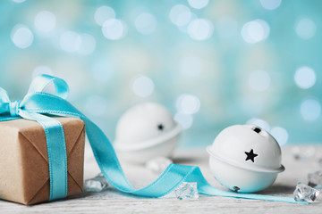 Christmas gift box and white jingle bell against turquoise bokeh background. Holiday greeting card. - obrazy, fototapety, plakaty