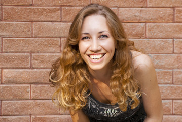 Photo of blonde girl with bright sincere smile on red brick back