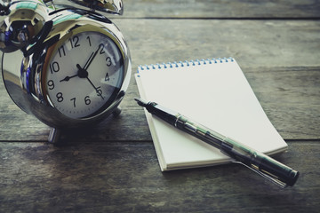 Time management concept: vintage tone alarm clock, pen and notep