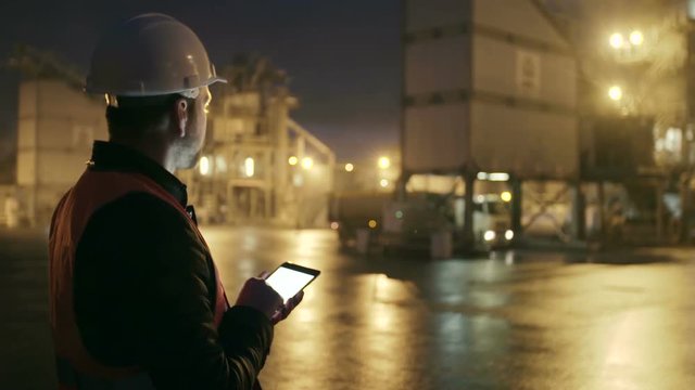 Engineer in hardhat checking the loading of truck with a tablet computer on heavy industry factory