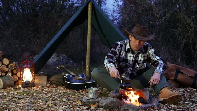 
4K.Man   in cowboy hat  near  bonfire make coffee. Autumn travel life. 
