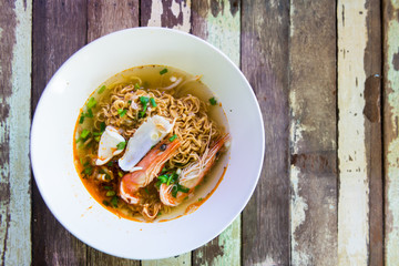 Spicy lemongrass soup with noodle and sea food in white bowl on wood table