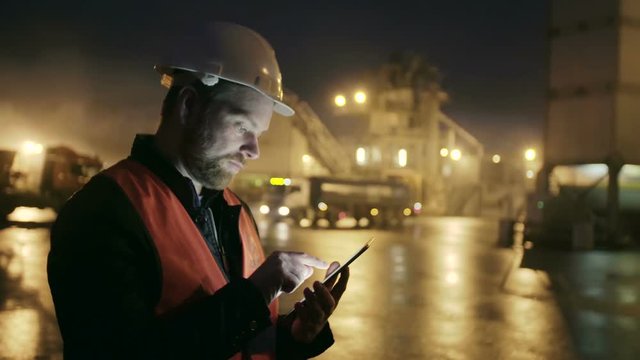 Engineer in hardhat with a tablet computer looks at truck on heavy industry factory