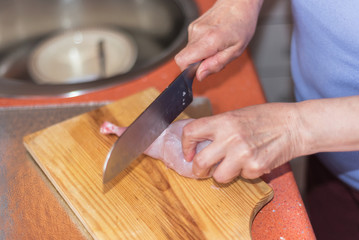 Senior woman hands cutting raw rabbit meat on a wodden table. Sh