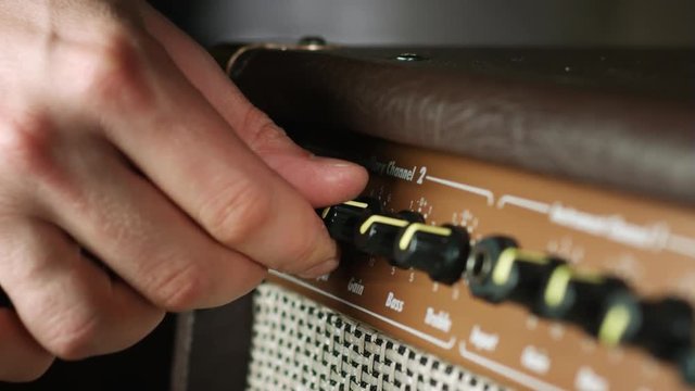 Close up of plugging electric guitar audio cable in amplifier jack and increase gain level