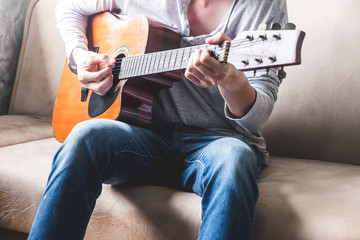 Casual young man playing guitar on sofa at home.