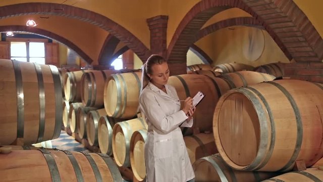 Winery technician in white robe controlling fermantation process of wine
