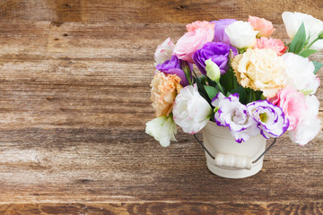 Pink, white and violet eustoma fresh flowers in pot on aged wooden background