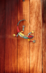 Colorful tin gecko on a dark red wood wall background © SailingAway