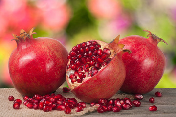 two whole pomegranate and half on the old wooden board with blurred garden background