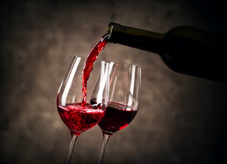 Naklejka na ściany i meble Red wine pouring into glass from bottle