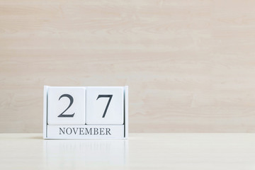Closeup surface white wooden calendar with black 27 november word on blurred brown wood desk and wood wall textured background with copy space , selective focus at the calendar