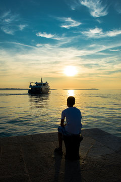 Junge auf Steg beobachtet abfahrendes Schiff bei Sonnenuntergang