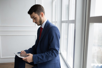 Businessman in white office using digital tablet sitting on windowsill