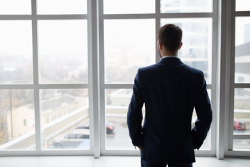 Fototapeta premium Businessman in white office thinking standing at window