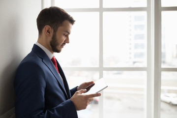 Fototapeta premium Businessman in white office using digital tablet at window