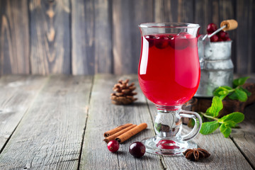 Fresh cranberry juice with cinnamon and anise in glass jars on the old wooden background. Selective focus.