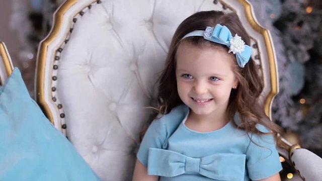 cheerful little girl in a blue dress sitting on chair