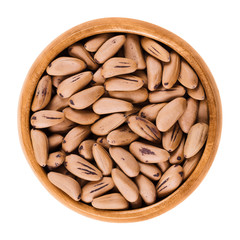 Stone pine seeds in wooden bowl. Fruits of Pinus pinea, also called the Italian, umbrella or parasol pine. Isolated macro food photo close up from above on white background.