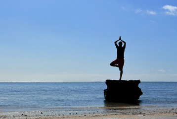 young man doing yoga on rock at the beach