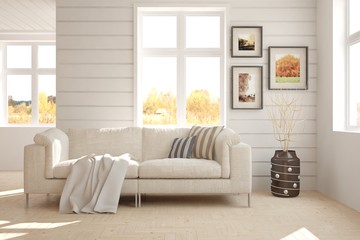 White room with sofa and autumn landscape in window. Scandinavian interior design