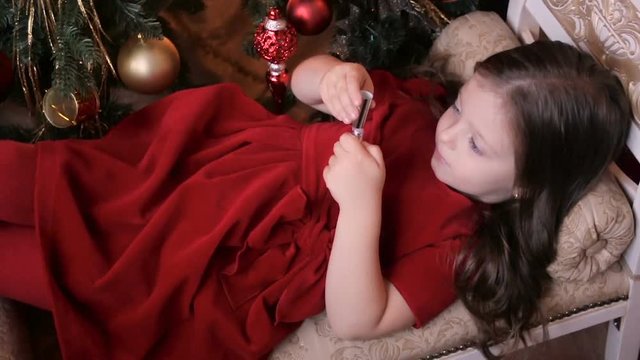 a little girl three years in a red dress lipstick lying on the couch next to the Christmas tree