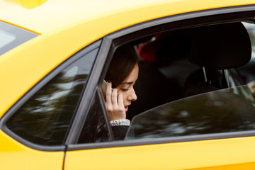 Naklejka premium Pensive brunette woman riding in taxi and talking on phone
