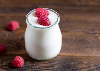 White yogurt with raspberries in glass bowl on rustic table.