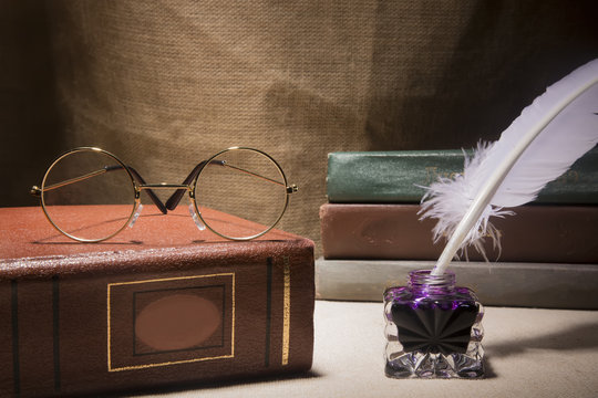 Vintage still life with glasses on old book near inkstand and feather on canvas background