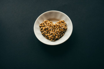 sprouted grains of wheat in shape of heart on white plate. black background with copy space. healthy food concept